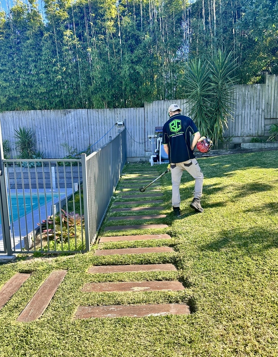 Brothers Gardenscape team member trimming a lawn edge beside timber stepping stones
